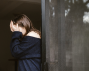 Woman with her head in her hands in a blue top standing up.